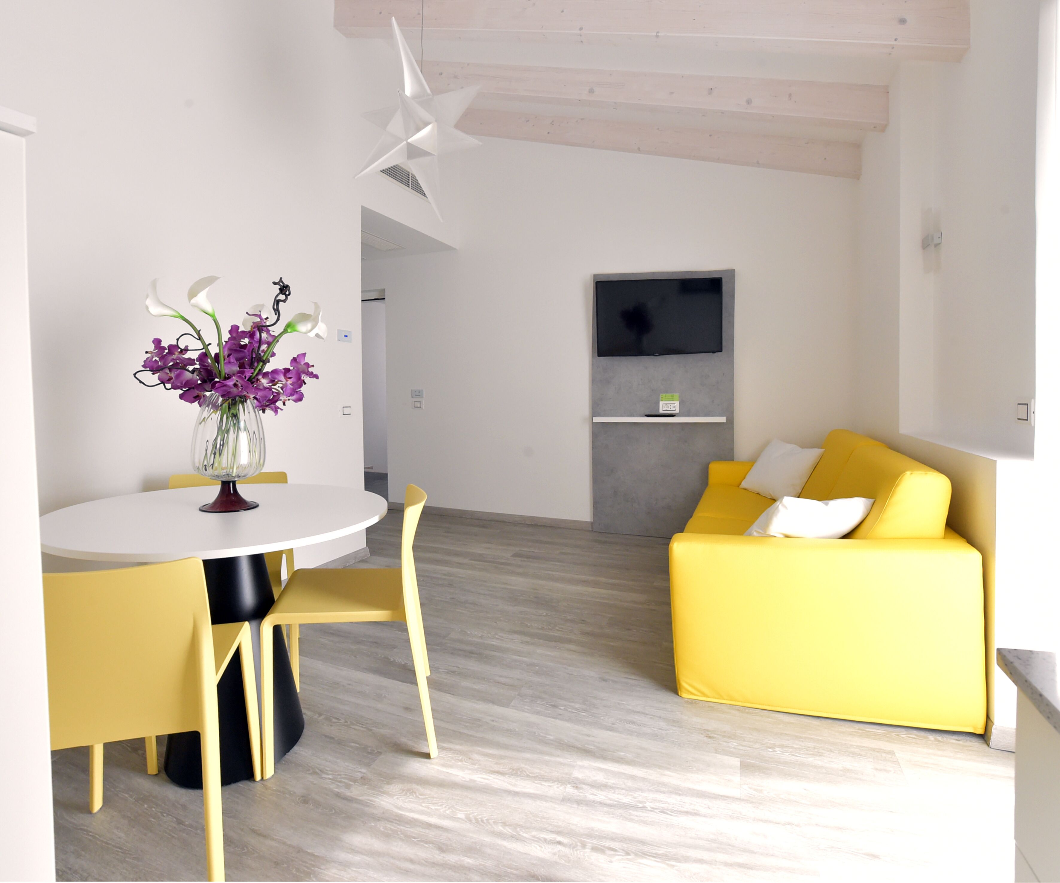 A modern living space with a dining area, a yellow sofa, and a flat-screen TV mounted on the wall.