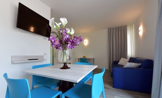 Uma sala de estar moderna com um sofá azul, uma mesa de jantar com cadeiras azuis e uma TV fixada na parede.