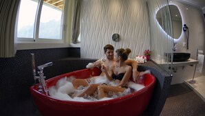 A red jacuzzi with a view of mountains through a window, a mirror, and a sink with a towel rack.