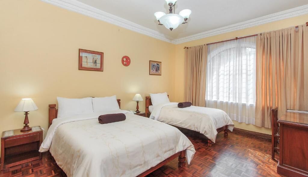 Une chambre d’hôtel avec deux lits, un plancher en bois, un lustre et des rideaux à la fenêtre.