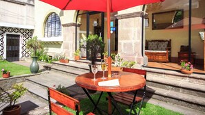 An outdoor patio with a round wooden table, two chairs, a red umbrella, and potted plants. - La Cartuja (Quito)