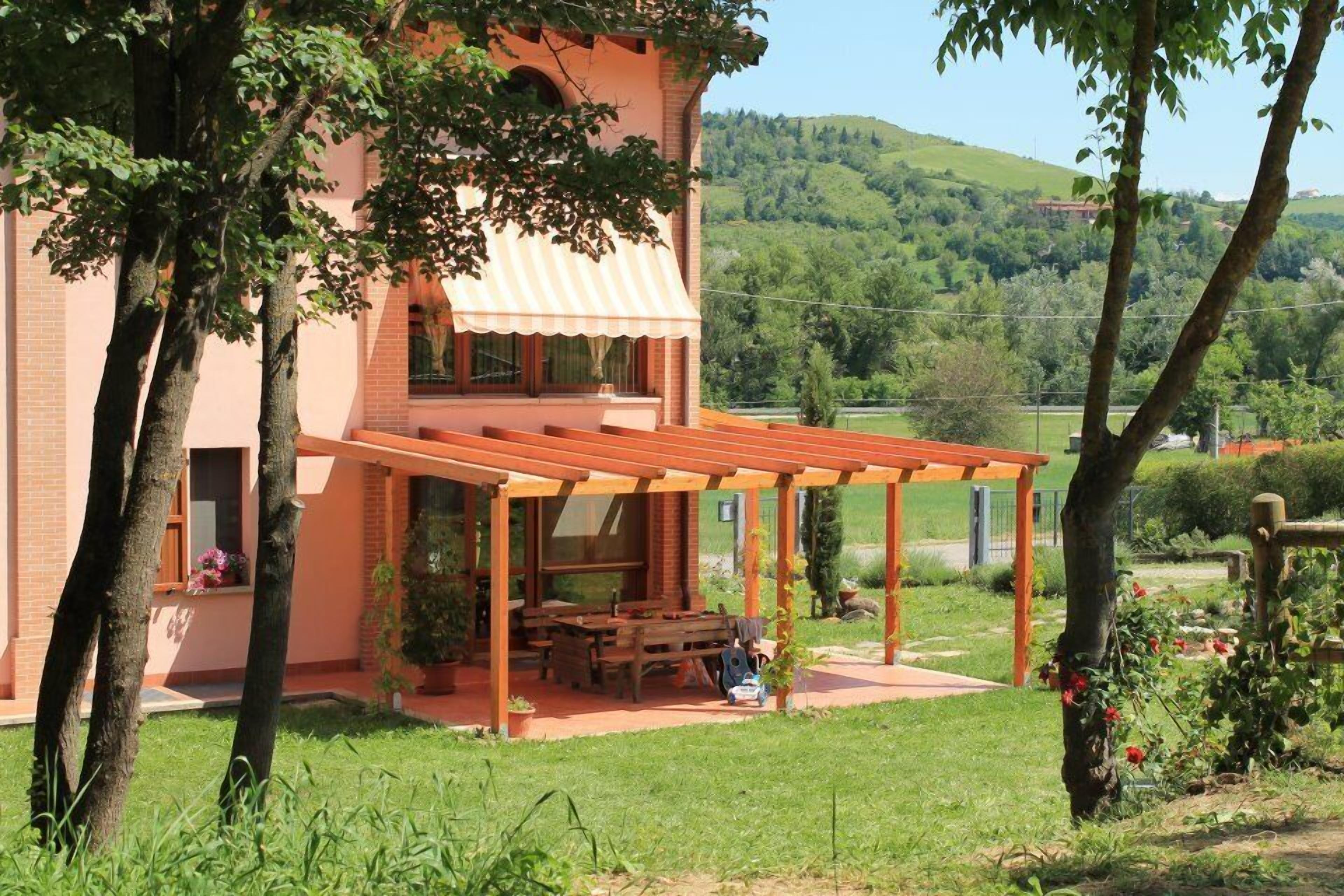 A two-story house with a covered patio, a brick exterior, and a view of a green hillside.