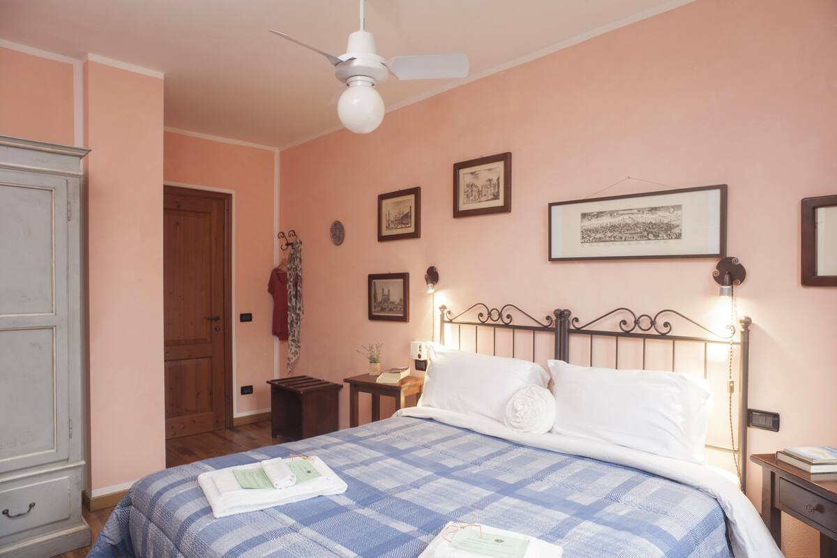 Une chambre à coucher comprenant un lit, un ventilateur de plafond, une table de chevet, une commode et des tableaux encadrés accrochés au mur.