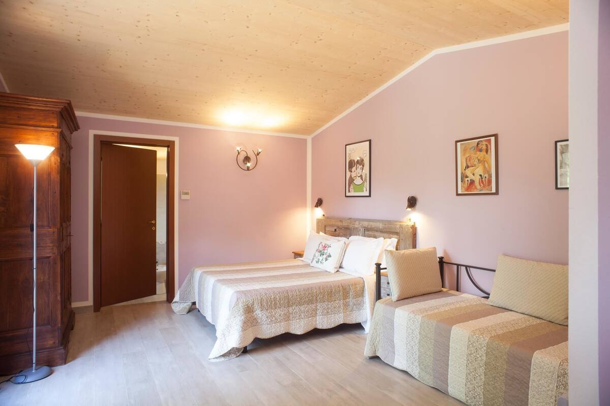 Une chambre avec deux lits, une armoire en bois et une porte donnant sur une autre pièce.