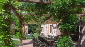 An outdoor patio area with a wooden table and benches, surrounded by greenery and a pergola structure. - Agriturismo Il Cavicchio (Pianoro)