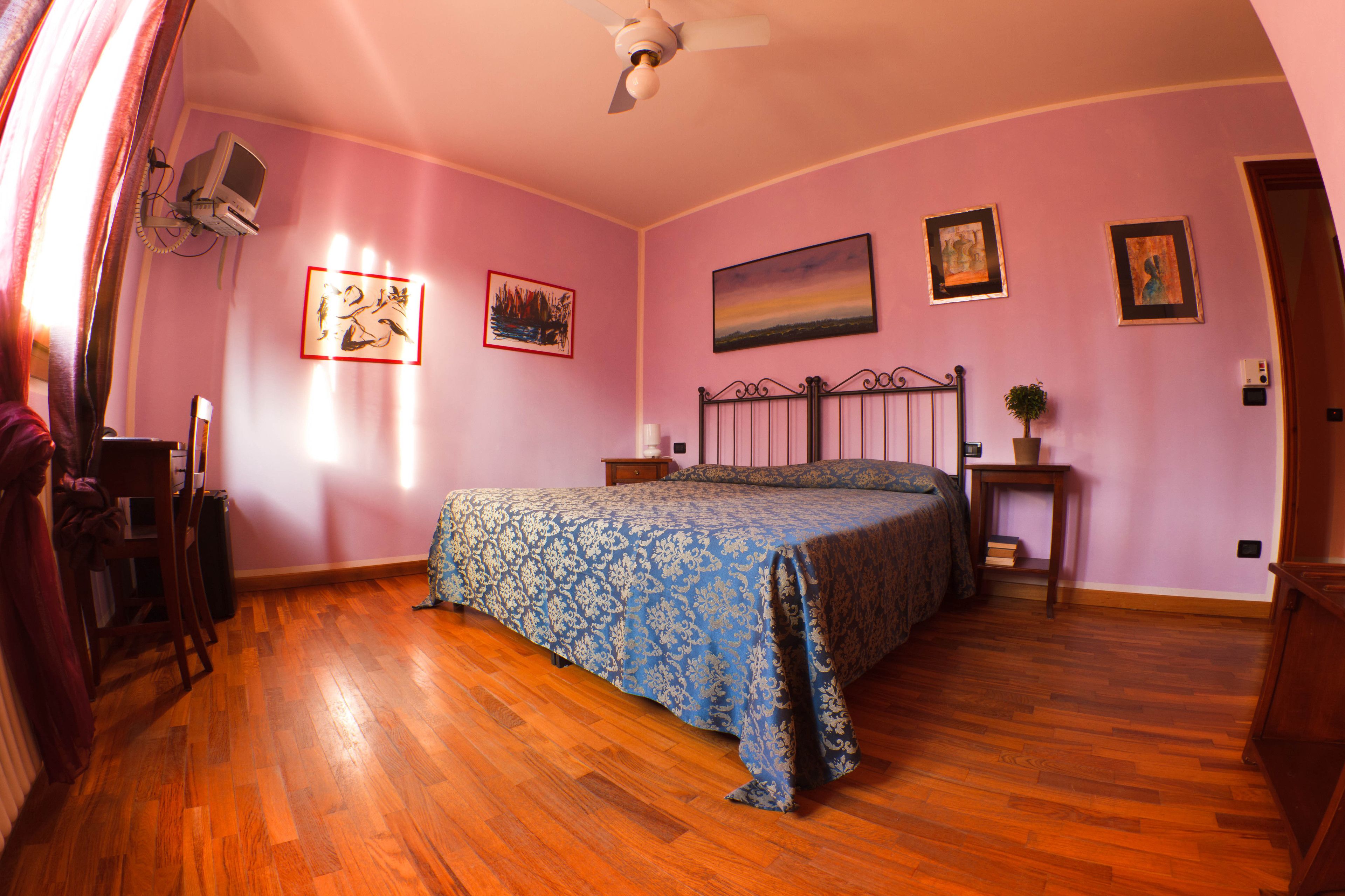 A bedroom with a bed, wooden floor, ceiling fan, and wall-mounted TV.