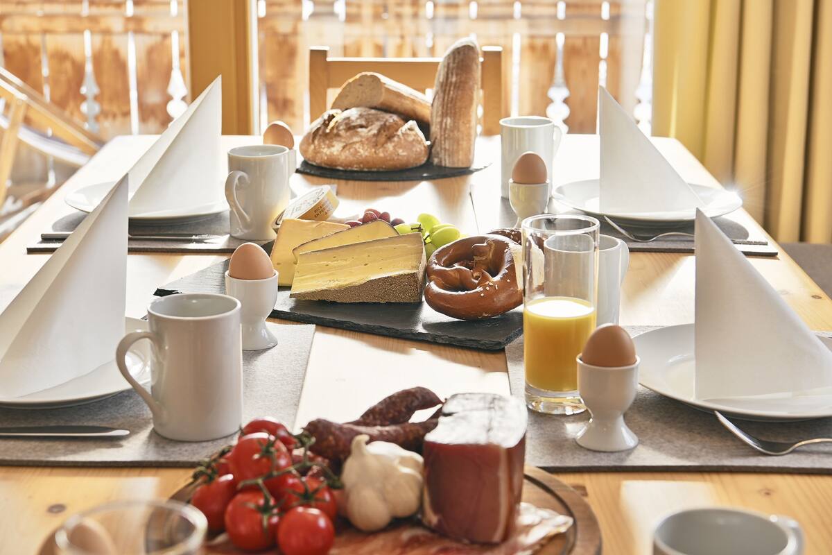 Un desayuno con pan, huevos, tomates y una tabla de quesos sobre una mesa de madera.