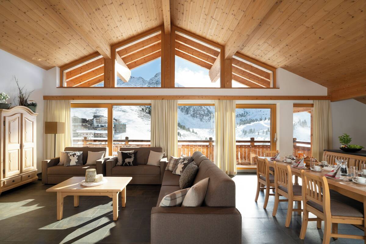Amplia sala de estar con techo alto, vigas de madera y ventanas grandes que ofrecen vistas a la montaña.