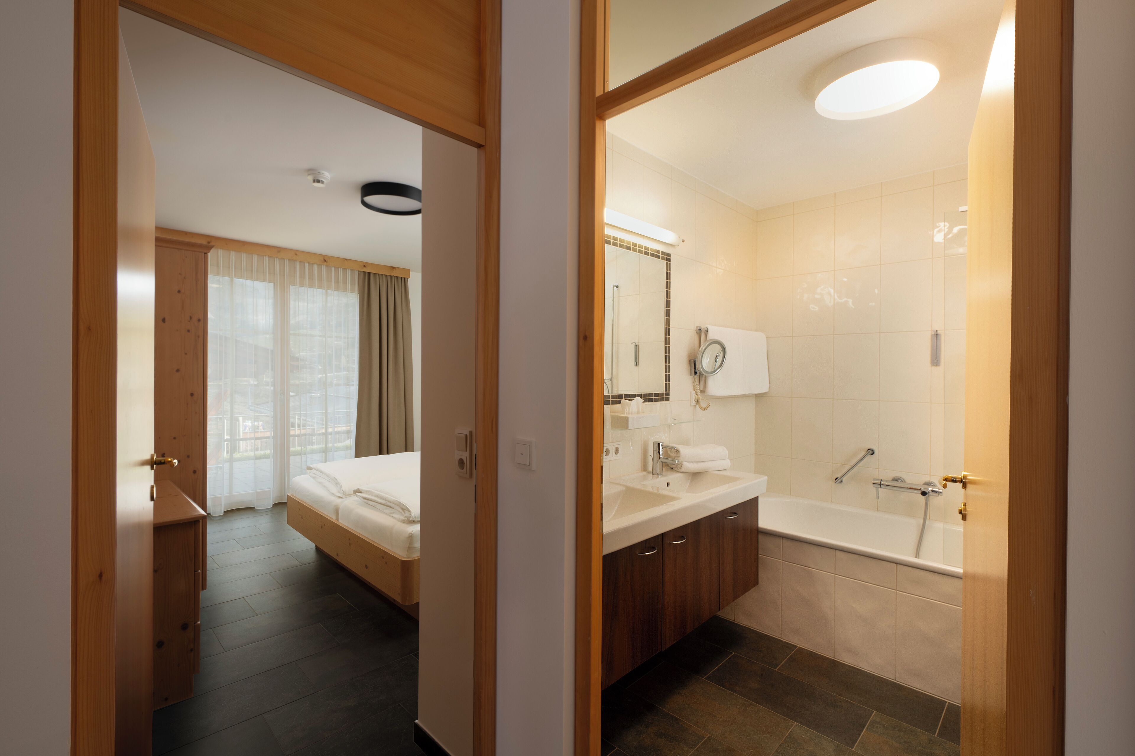 A modern hotel room with a bed, a bathroom with a bathtub, and a large window with curtains.