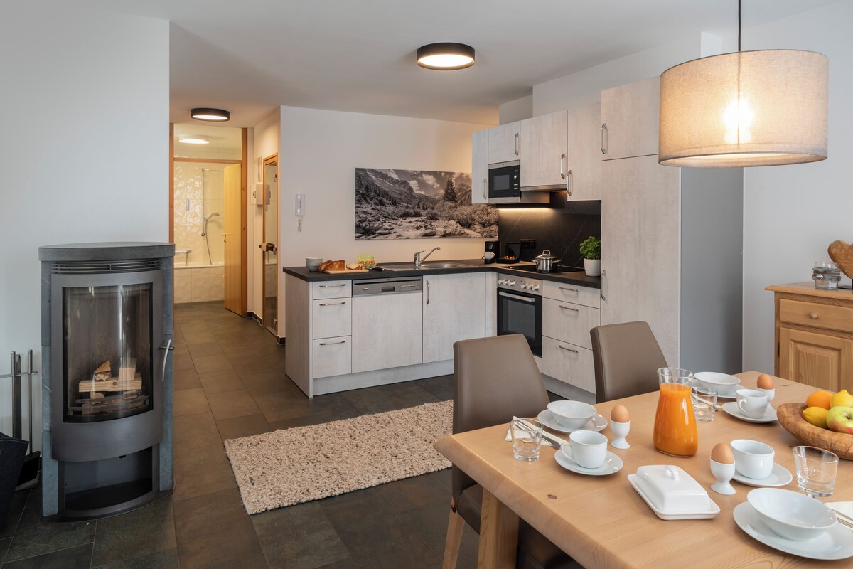 A modern kitchen with a central island, a dining area with a wooden table set for breakfast, and a cozy fireplace.