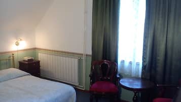Quarto de hotel com uma cama, uma escrivaninha com telefone, uma cadeira e uma mesinha.