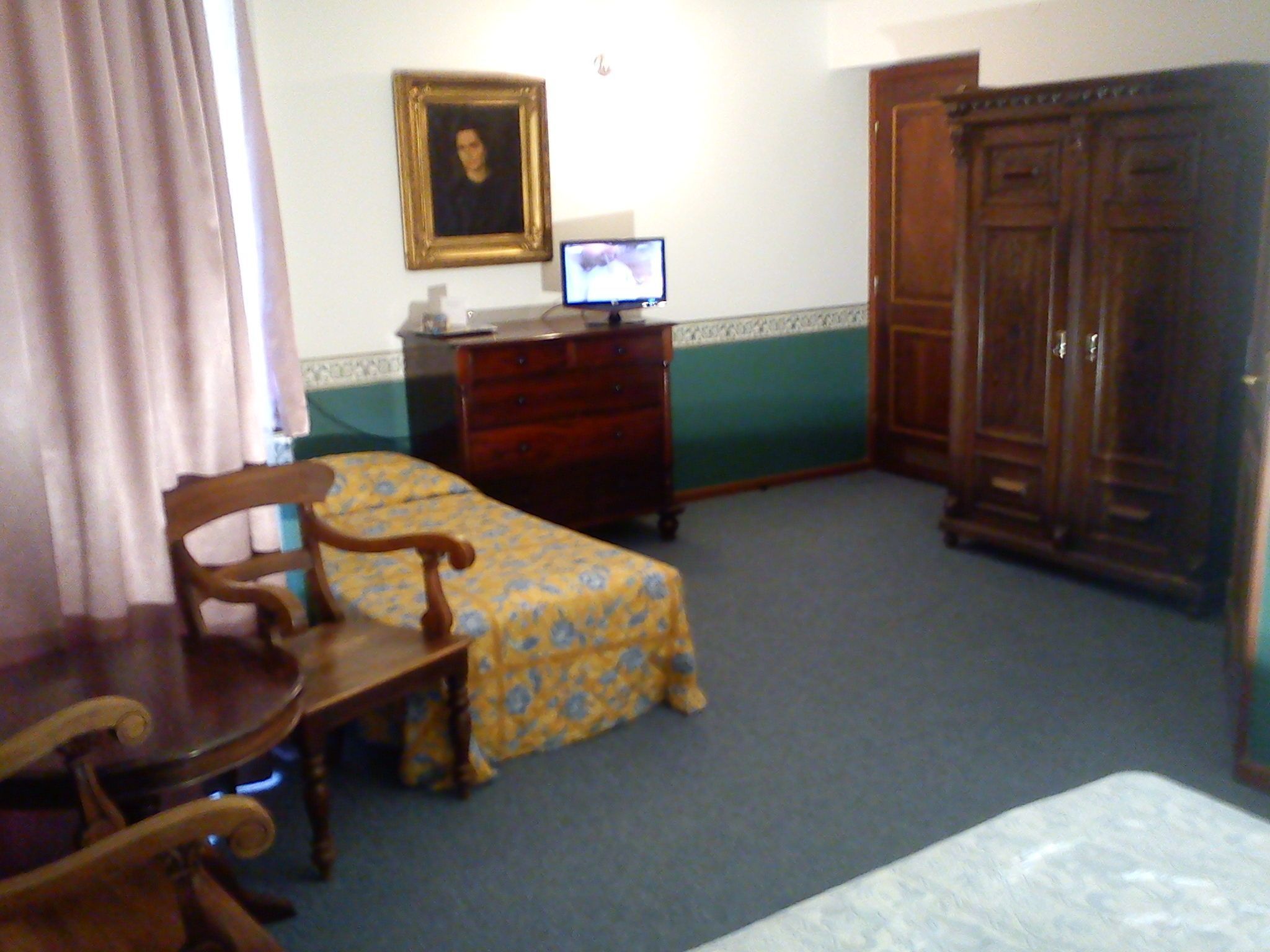 Una habitación con cama, una silla de madera, un escritorio, un aparador y un televisor.