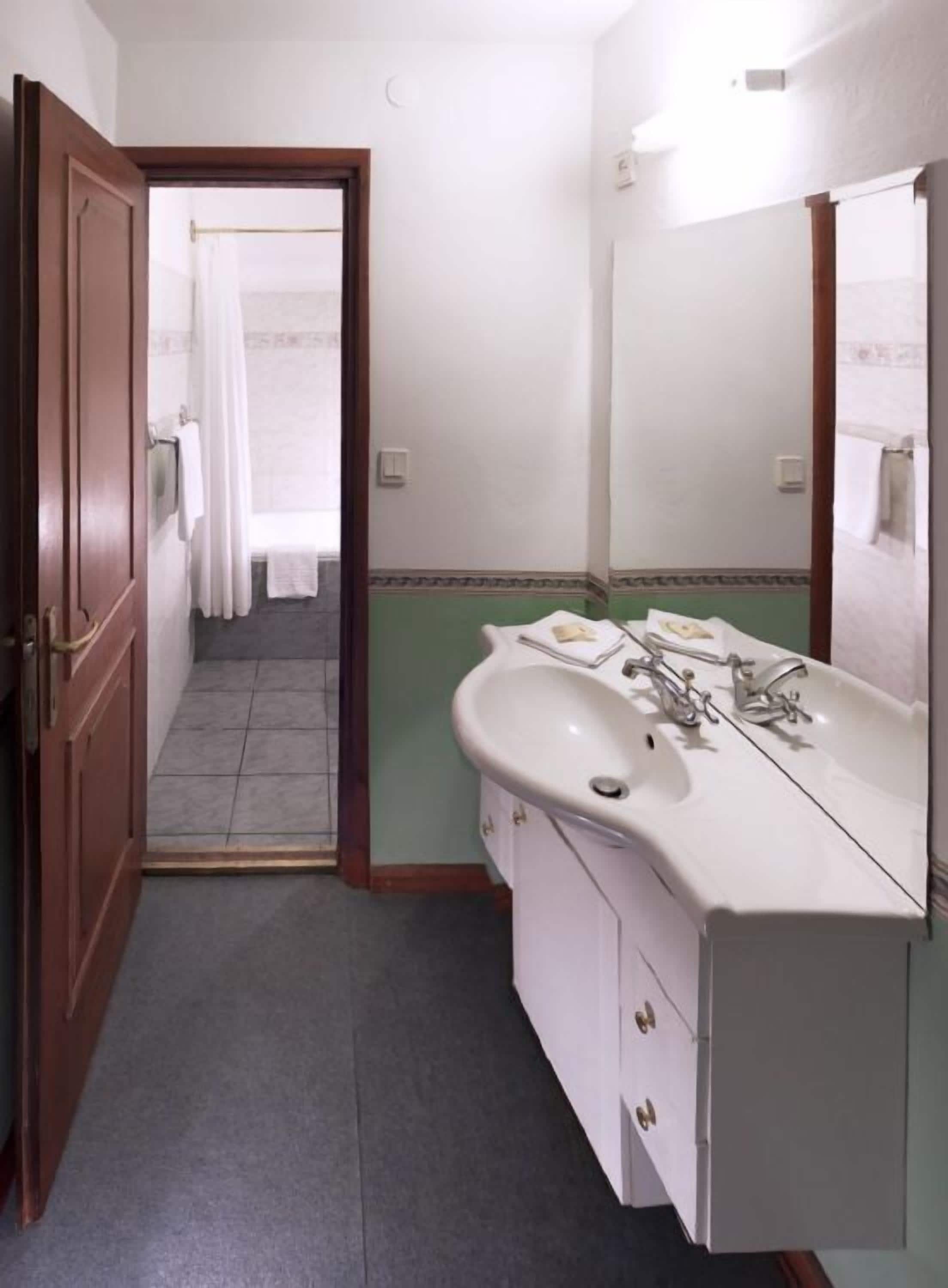 A bathroom with a white sink, two mirrors, and a door leading to a shower area.