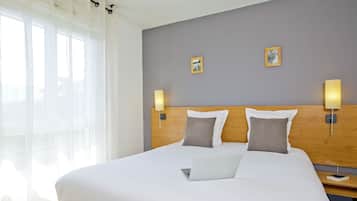 A neatly made bed with a laptop, two wall-mounted lamps, and a small picture frame on a grey wall.