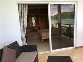 Una habitación con puerta corrediza de vidrio que da a un balcón con vistas a la playa y al bosque.