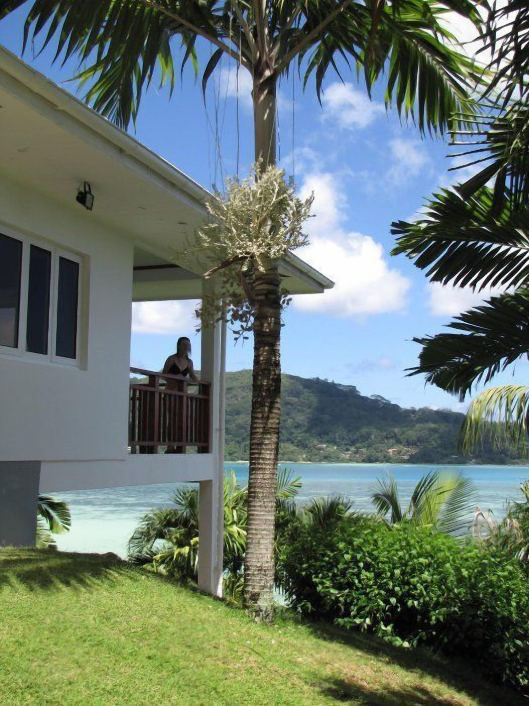 A house with a balcony overlooking a coastal area with a view of the sea and hills.