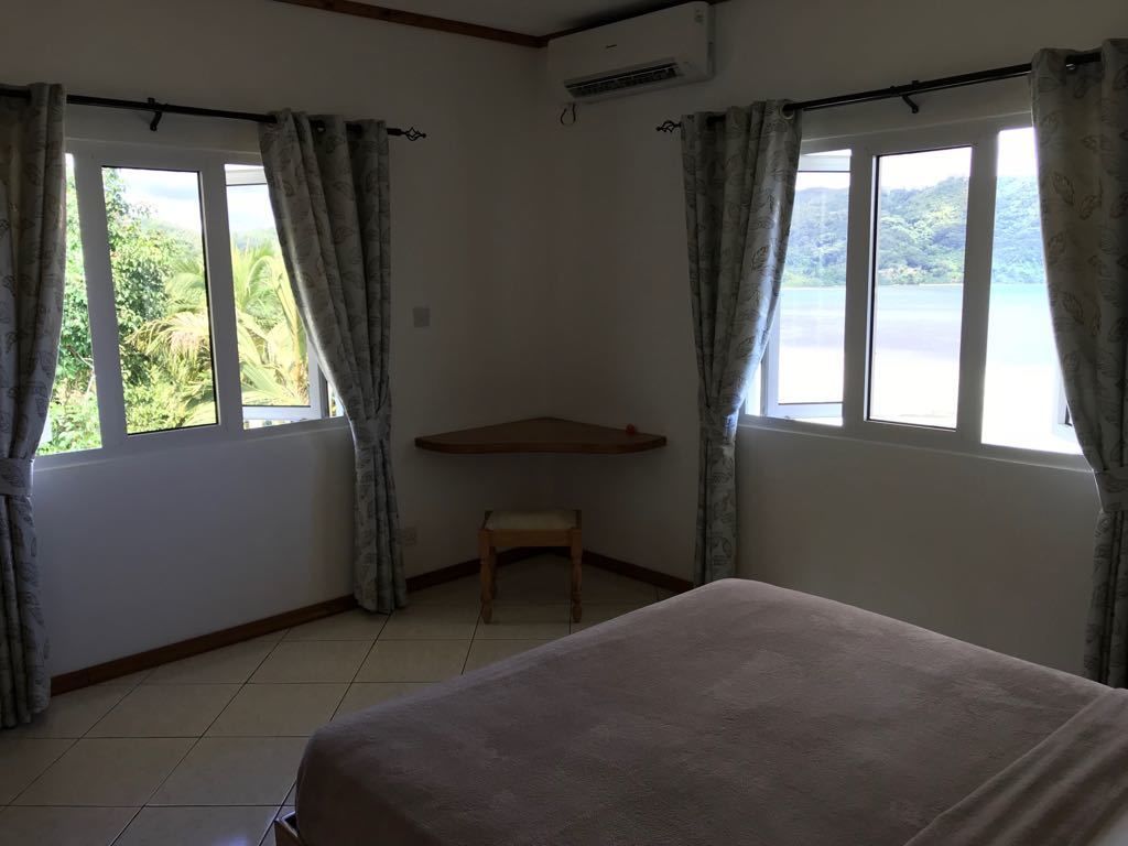 Une pièce comprenant un lit, une petite table et une chaise. Il y a des fenêtres avec des rideaux, et un appareil de climatisation est fixé au mur.
