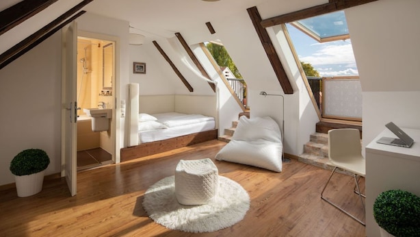 Un dormitorio tipo loft con piso de madera, una cama blanca, un escritorio con una computadora portátil y vistas al cielo a través de un tragaluz.