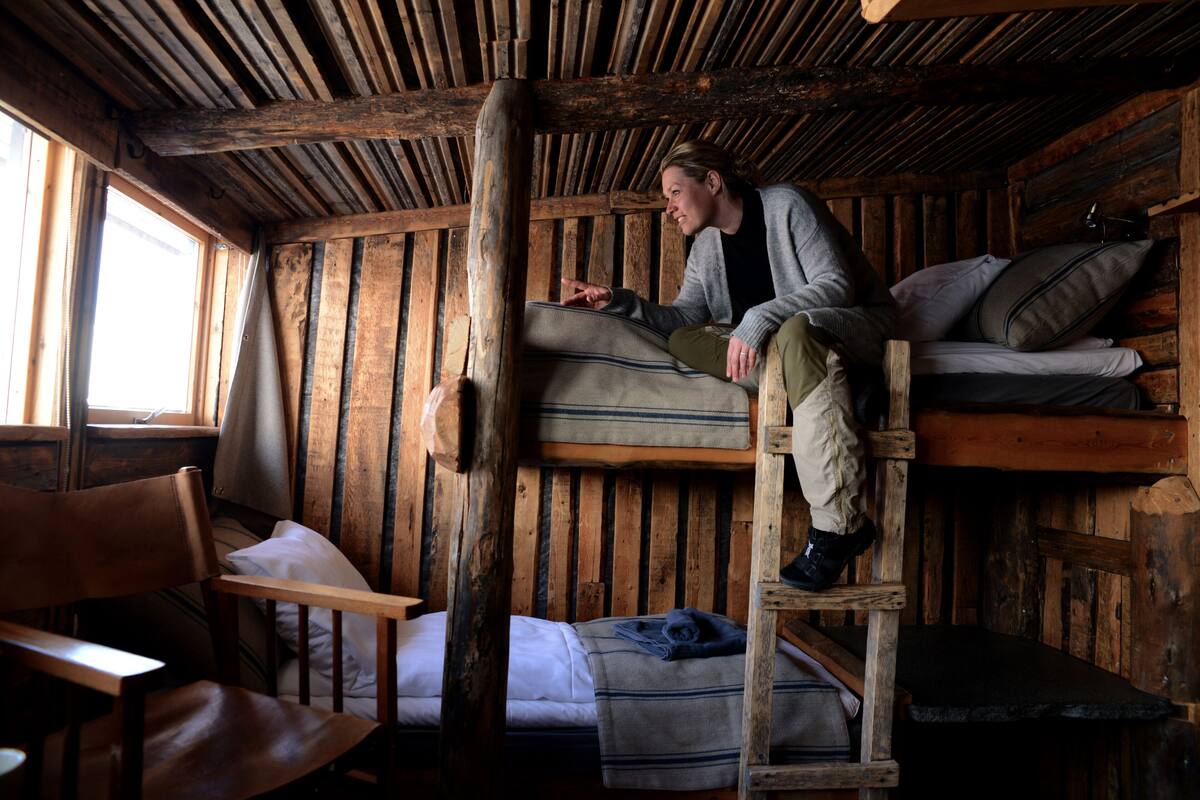 A rustic cabin interior with a bunk bed, wooden walls, a ladder, and a chair.