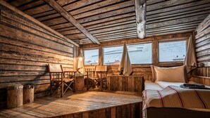 Une chambre de style cabane avec des murs et des planchers en bois, un lit recouvert d’une couverture à rayures, un bureau avec une lampe et une fenêtre donnant sur des immeubles.