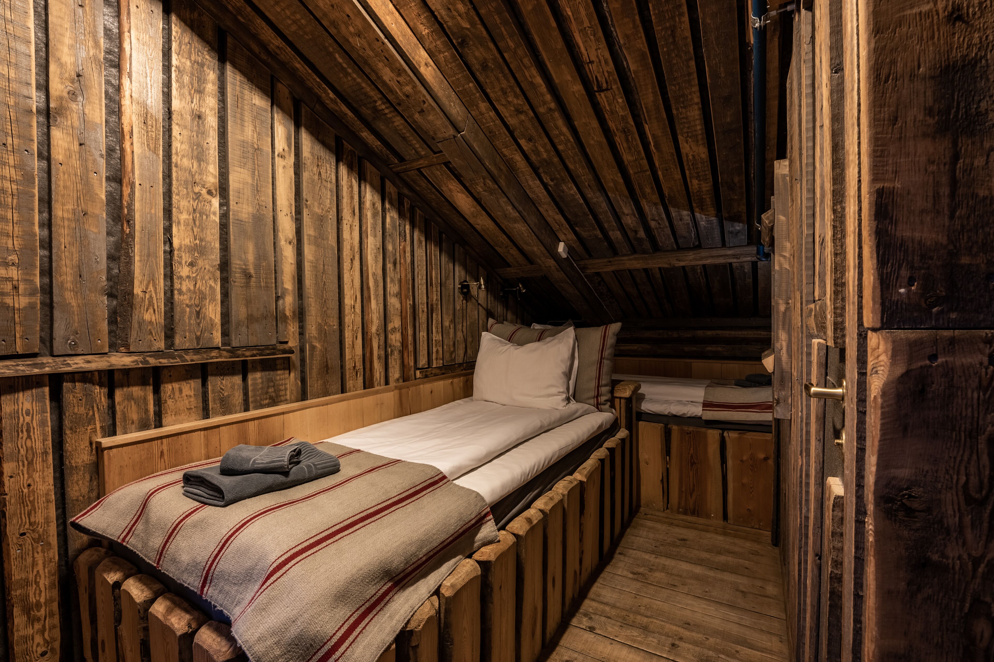 Una cabaña rústica de madera con una cama individual, una escalera de madera y un ventanal pequeño.