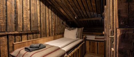 Una cabaña rústica de madera con una cama individual, una escalera de madera y un ventanal pequeño.