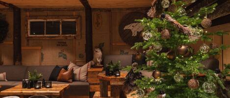 A cozy room with a wooden ceiling, a Christmas tree, a sofa, and a decorative wall.