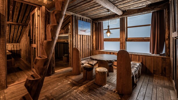 L’intérieur d’un chalet rustique, avec un escalier en bois, une table à manger et une grande fenêtre agrémentée de rideaux.