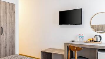 Ein modernes Hotelzimmer mit einem Holzschrank, einem flachbildfernseher an der Wand, einem Schreibtisch mit Stuhl und einer kleinen Küchenzeile.