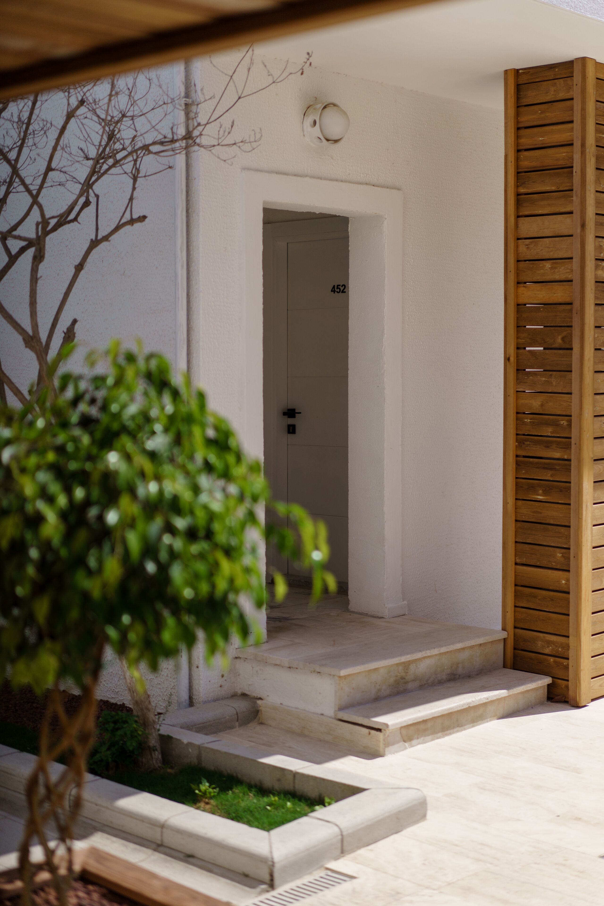 A modern entrance with a wooden door marked "452" and a concrete staircase leading to a white door.