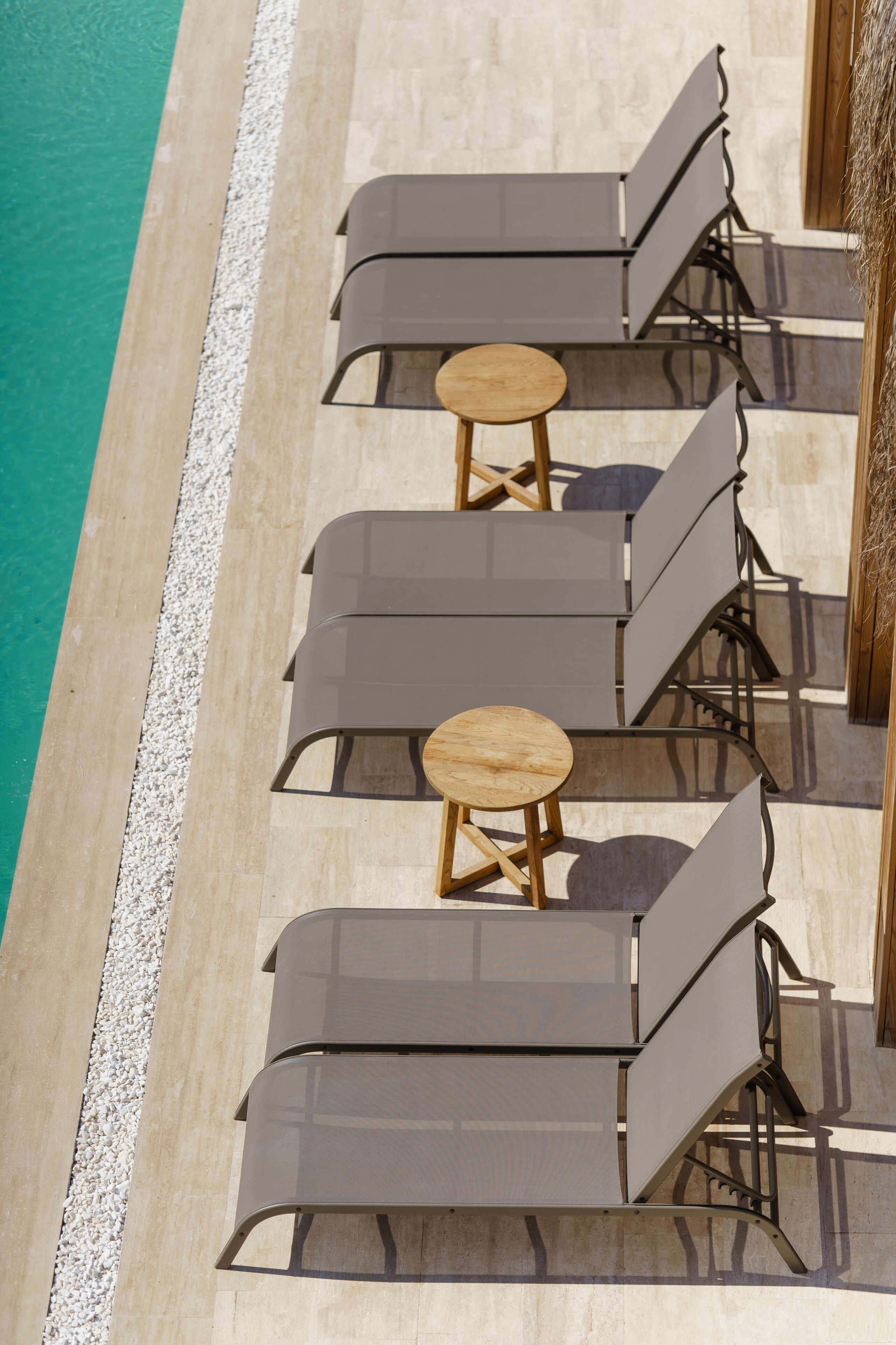 A poolside area with multiple lounge chairs and small round tables, arranged in a row along the edge of a pool.
