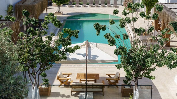 A pool area with lounge chairs and a table, surrounded by potted plants and a thatched roof structure. - Costa Maya Hotel (Bodrum)