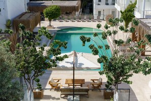 A pool area with lounge chairs and a table, surrounded by potted plants and a thatched roof structure.