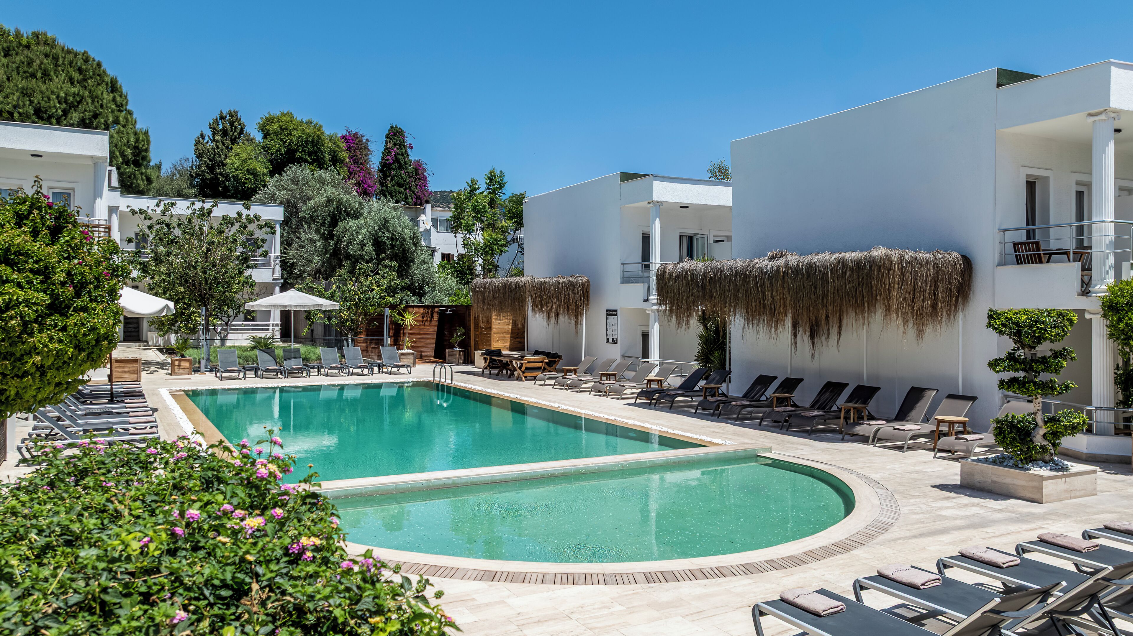 A pool area with lounge chairs, a thatched roof, and a clear blue sky.