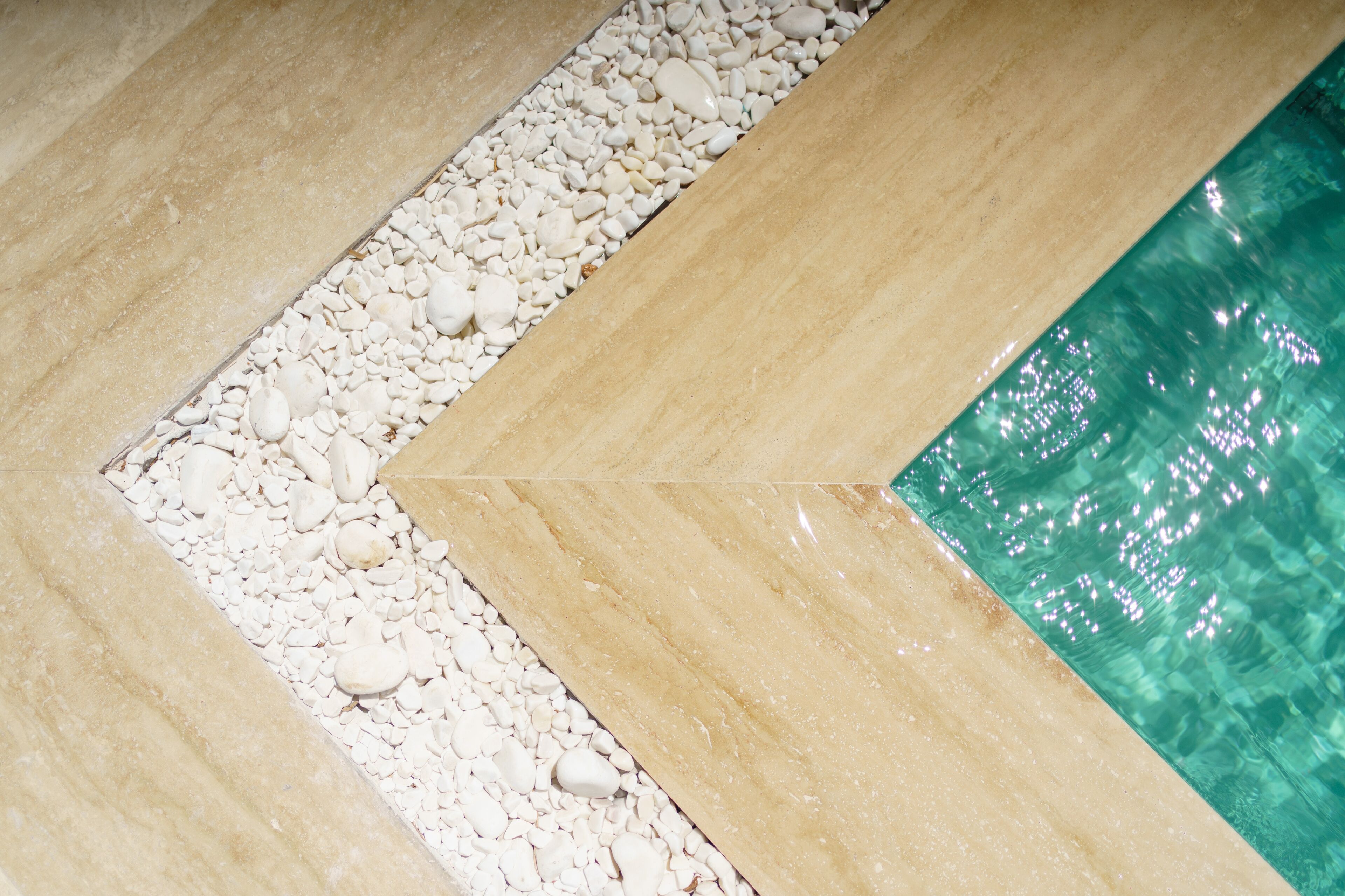 A tiled floor with a pebble border and a section of clear water.