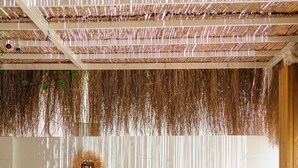 A room with a woven ceiling, a white wall with two circular wall decorations, a wooden table with chairs, and a patterned floor. - Costa Maya Hotel (Bodrum)