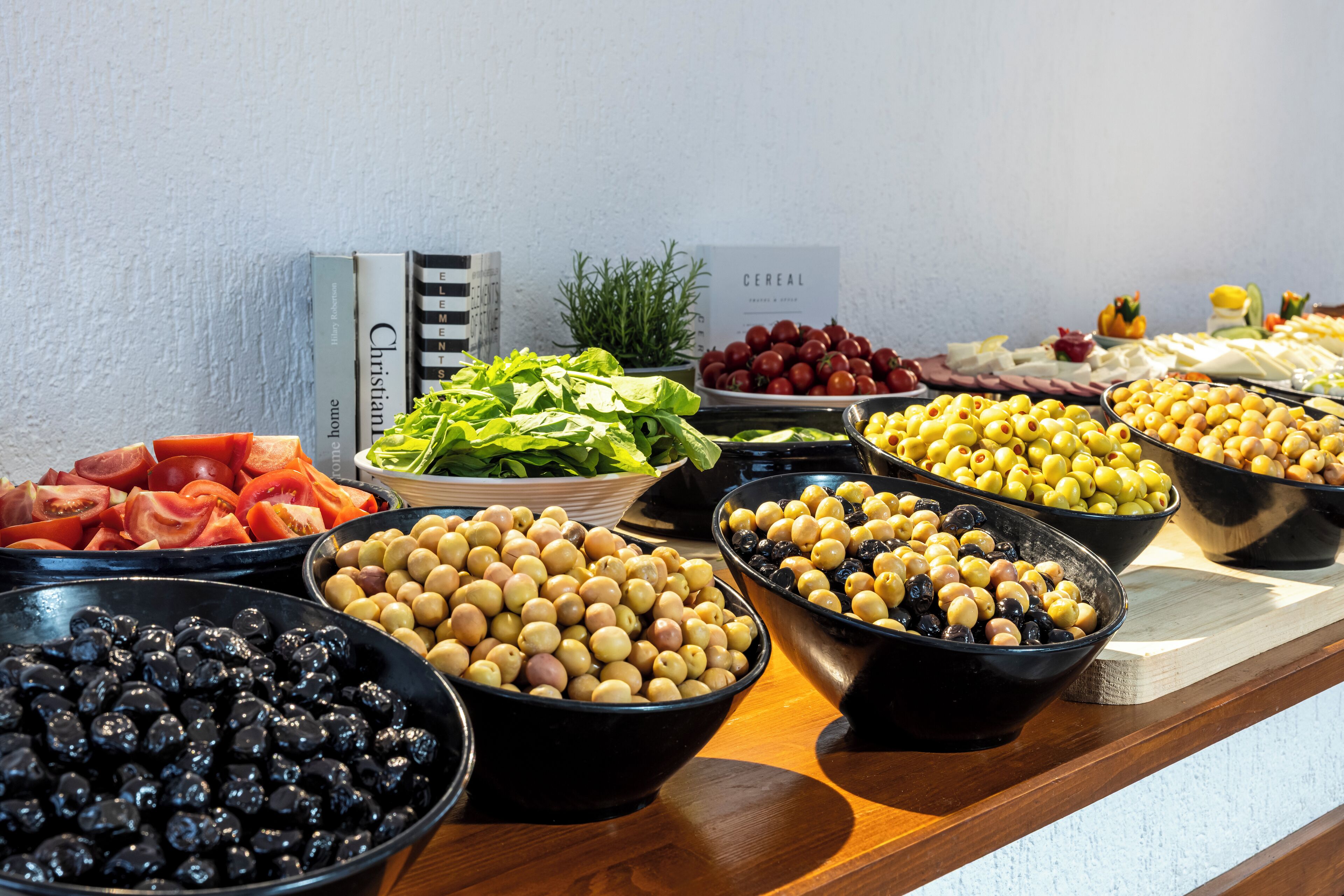 A buffet table with various food items including olives, tomatoes, and leafy greens.