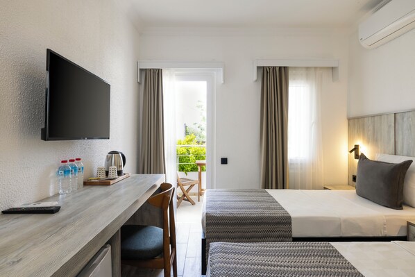 A hotel room with a bed, a desk with a TV, a chair, a table with a kettle, and a window with curtains.