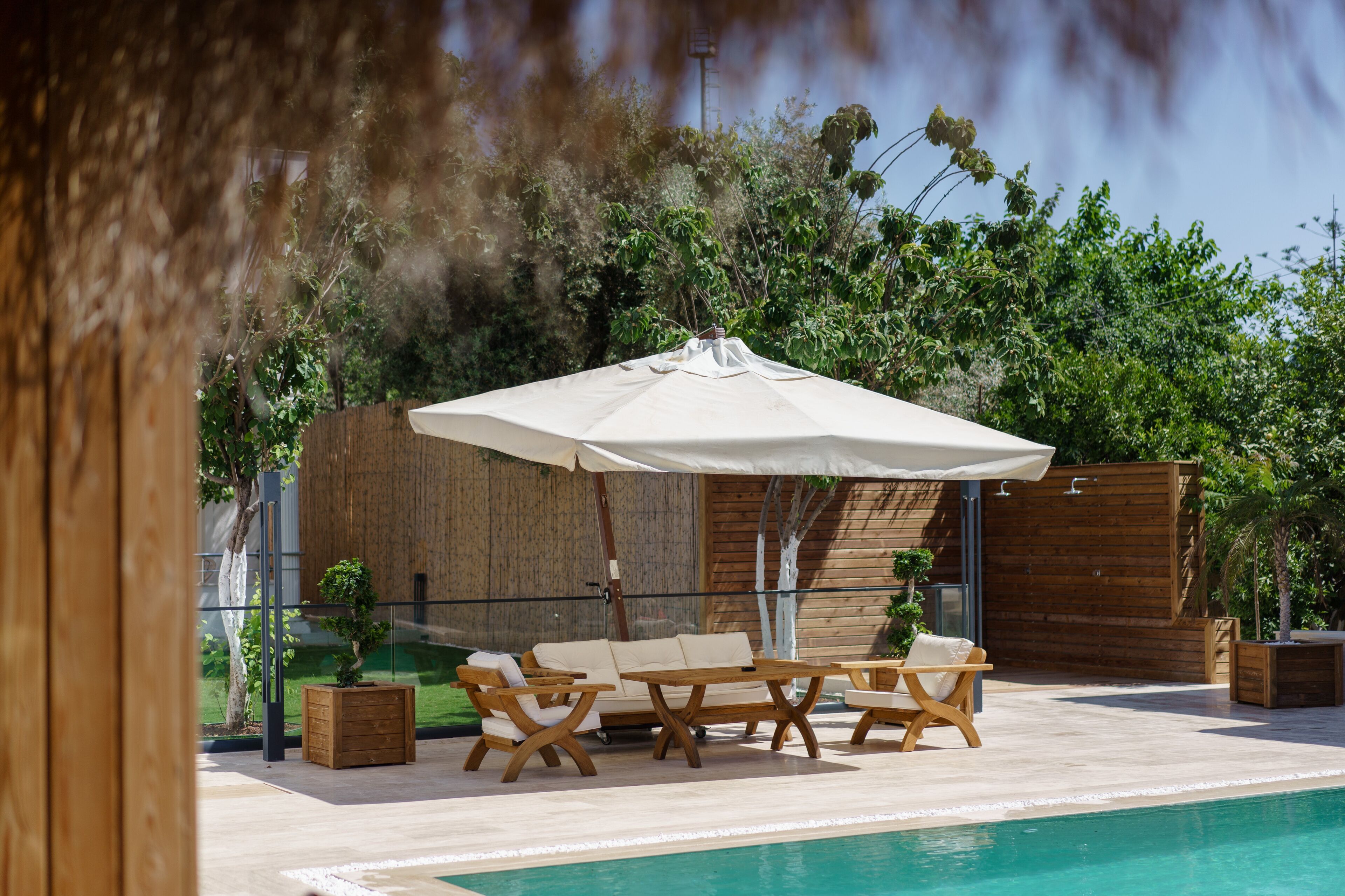 A poolside area with a wooden deck, a white umbrella, and a seating arrangement including a sofa and chairs.