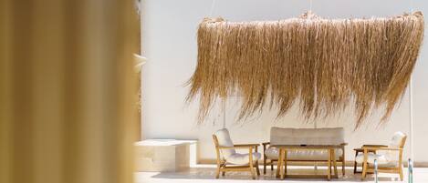 A poolside area with a hanging thatch, wooden lounge chairs, and a table.