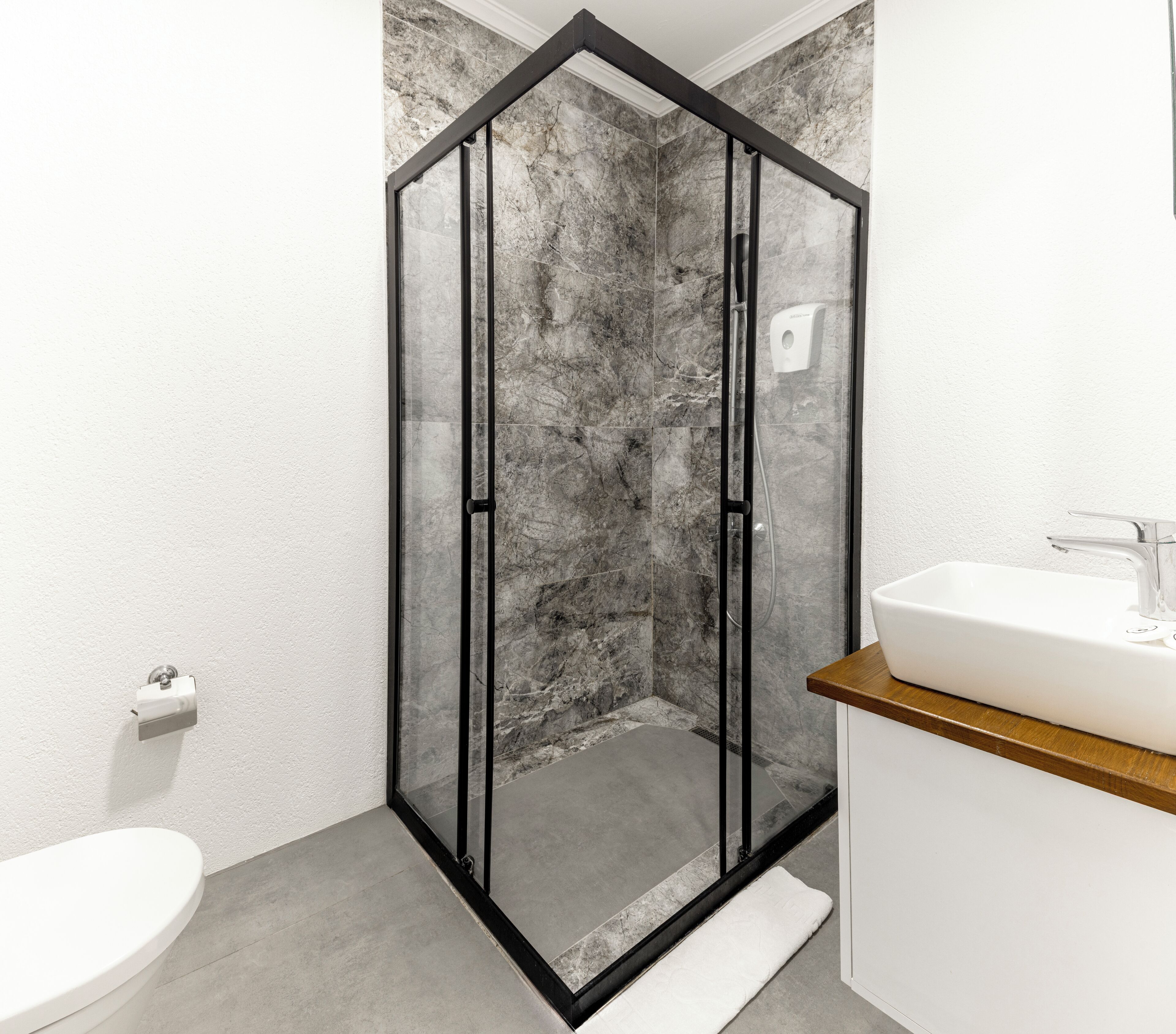 A modern bathroom with a glass-enclosed shower, a white sink, and a marble-tiled wall.
