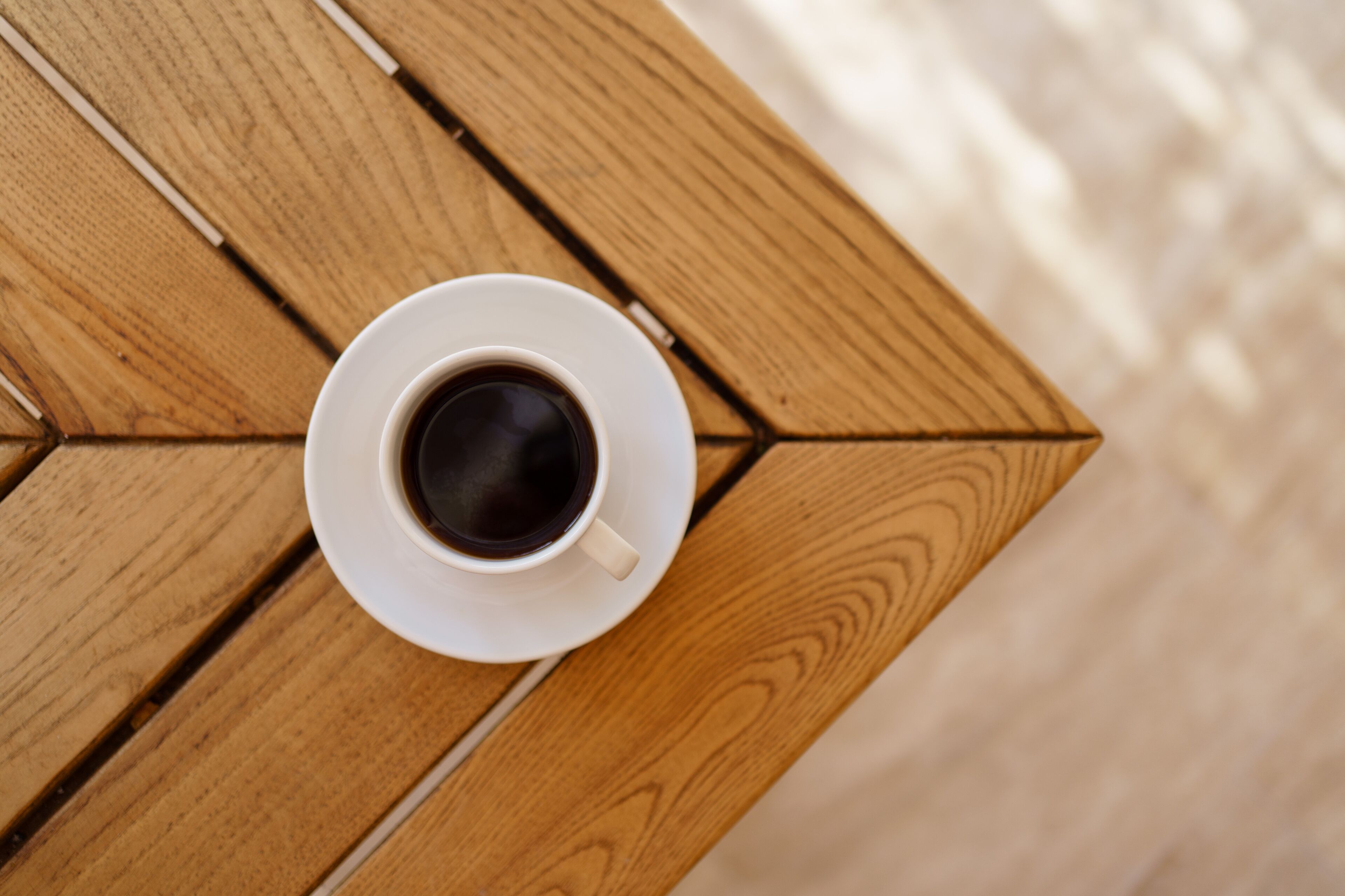 A white cup of coffee on a wooden table with a geometric pattern.