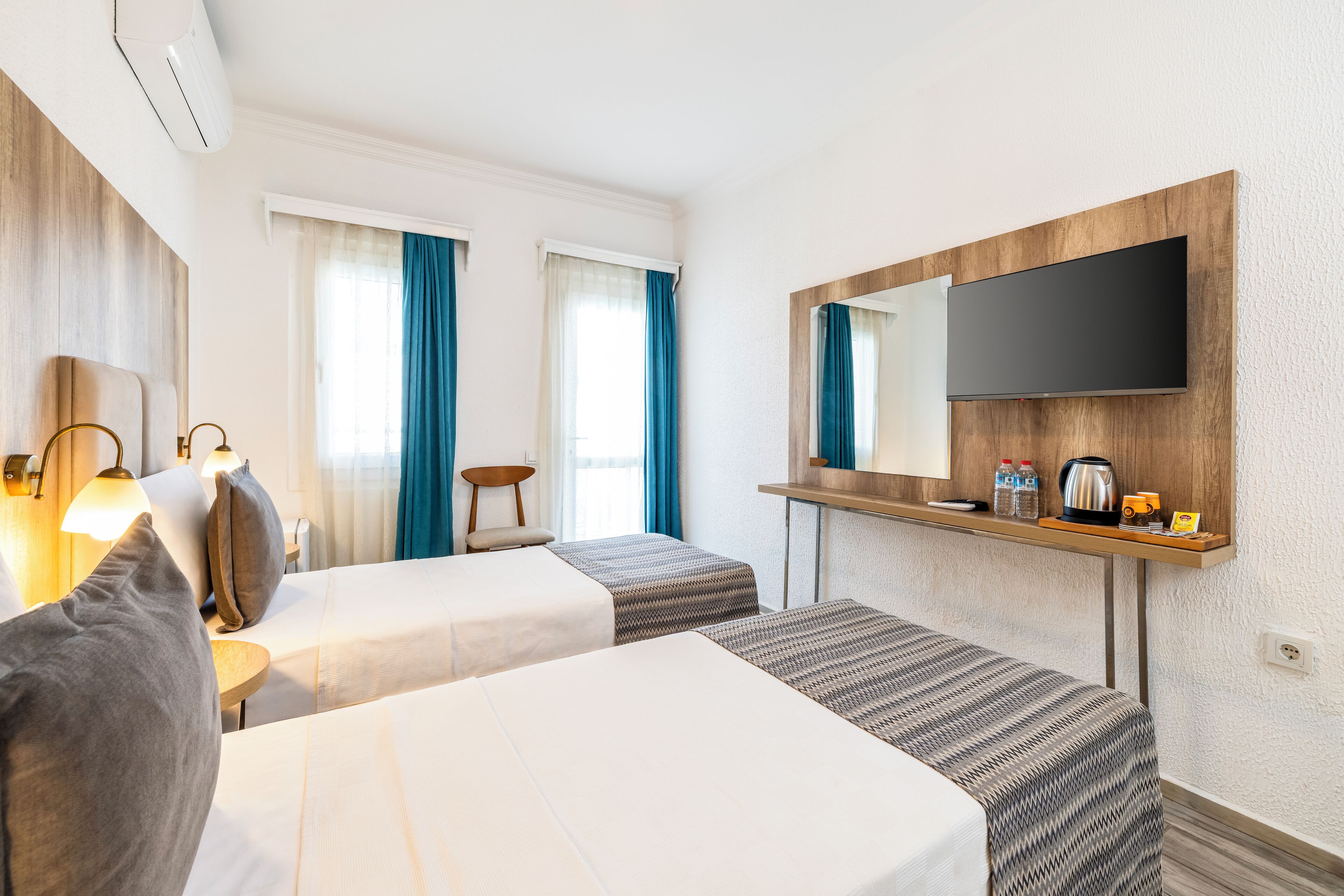 Een hotelkamer met twee bedden, een tv aan de muur, een klein tafeltje met een waterkoker en een stoel.