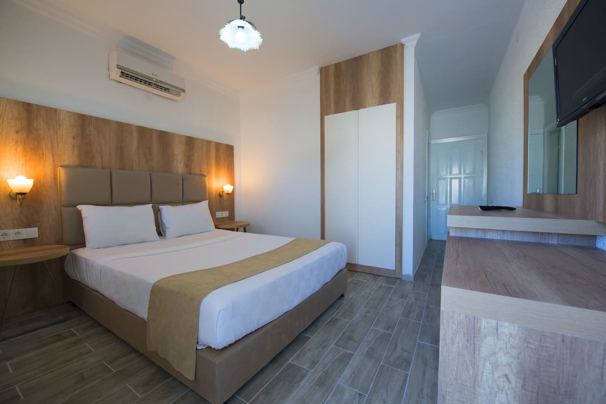 A modern hotel room with a large bed, bedside lamps, a wooden headboard, a built-in TV, and a wardrobe.
