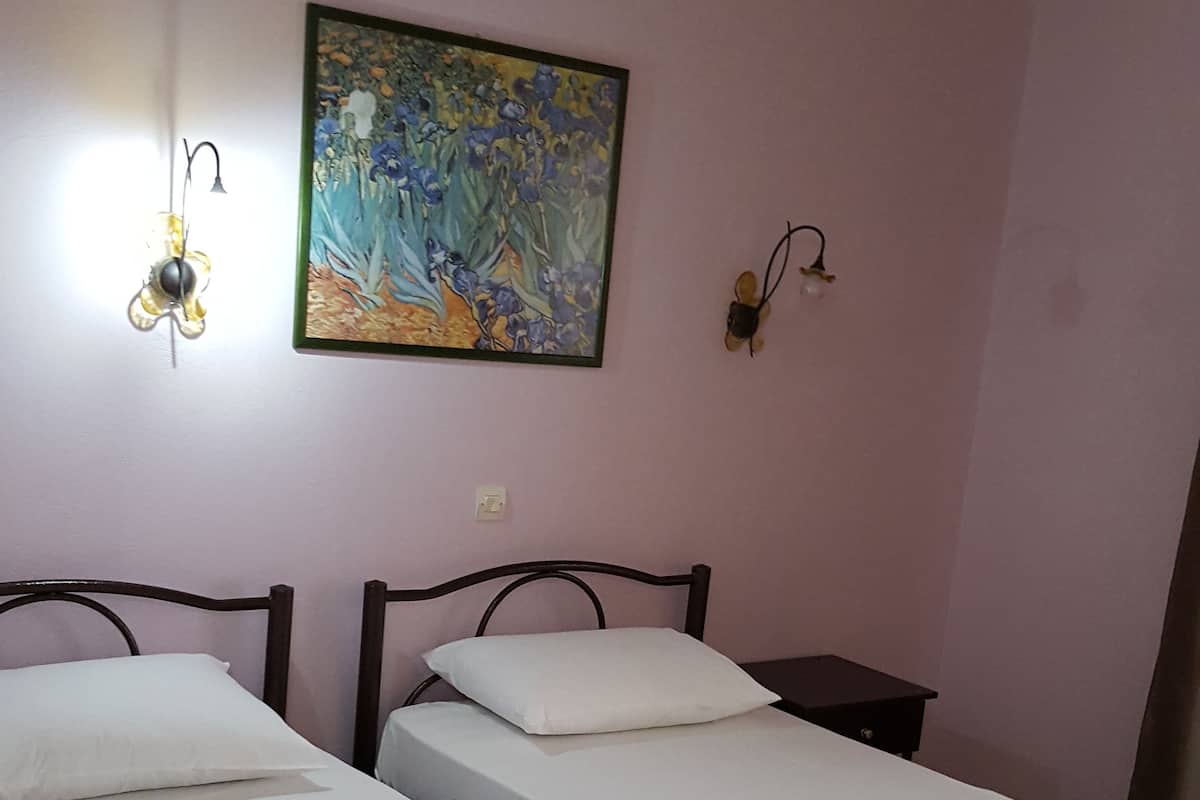 A room with two single beds, a nightstand, a wall-mounted lamp, and a painting.