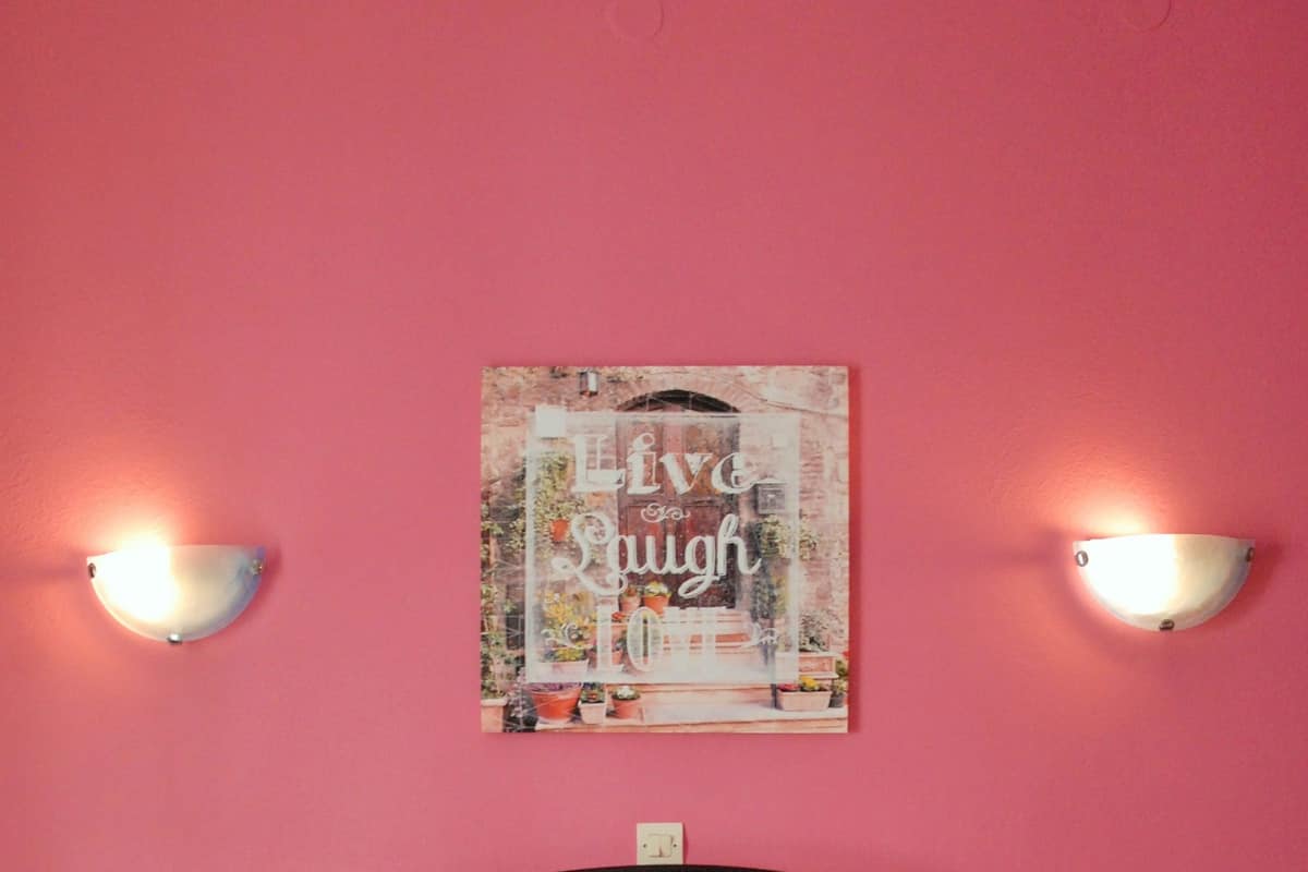 A bed with white linens, a pink wall, and two wall-mounted lights.