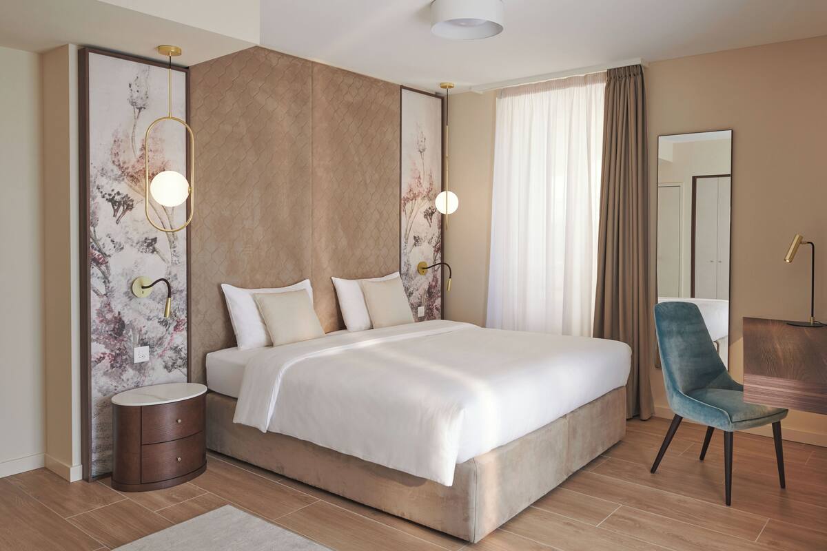 Una habitación de hotel moderna con una cama grande, una mesita de noche, una silla y un espejo amplio.