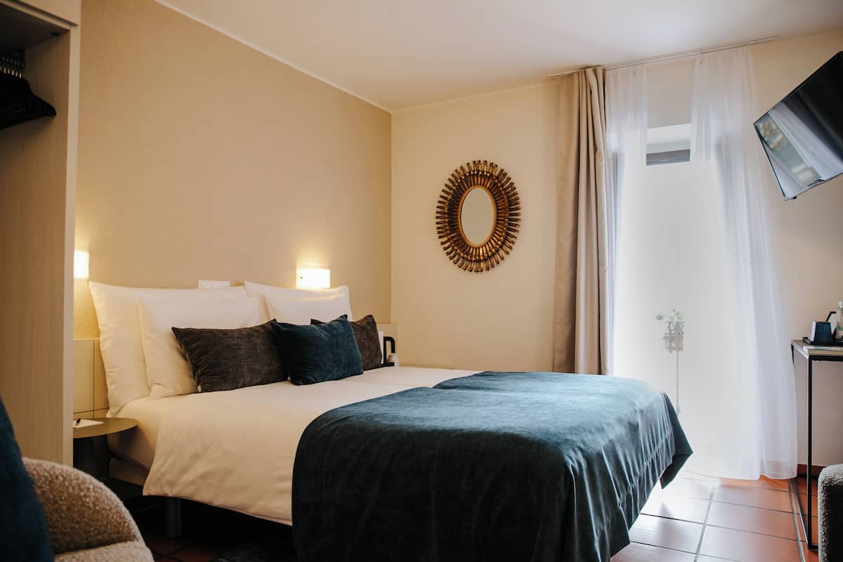 Habitación de hotel con cama, mesita de noche, espejo en la pared y ventana con cortinas.