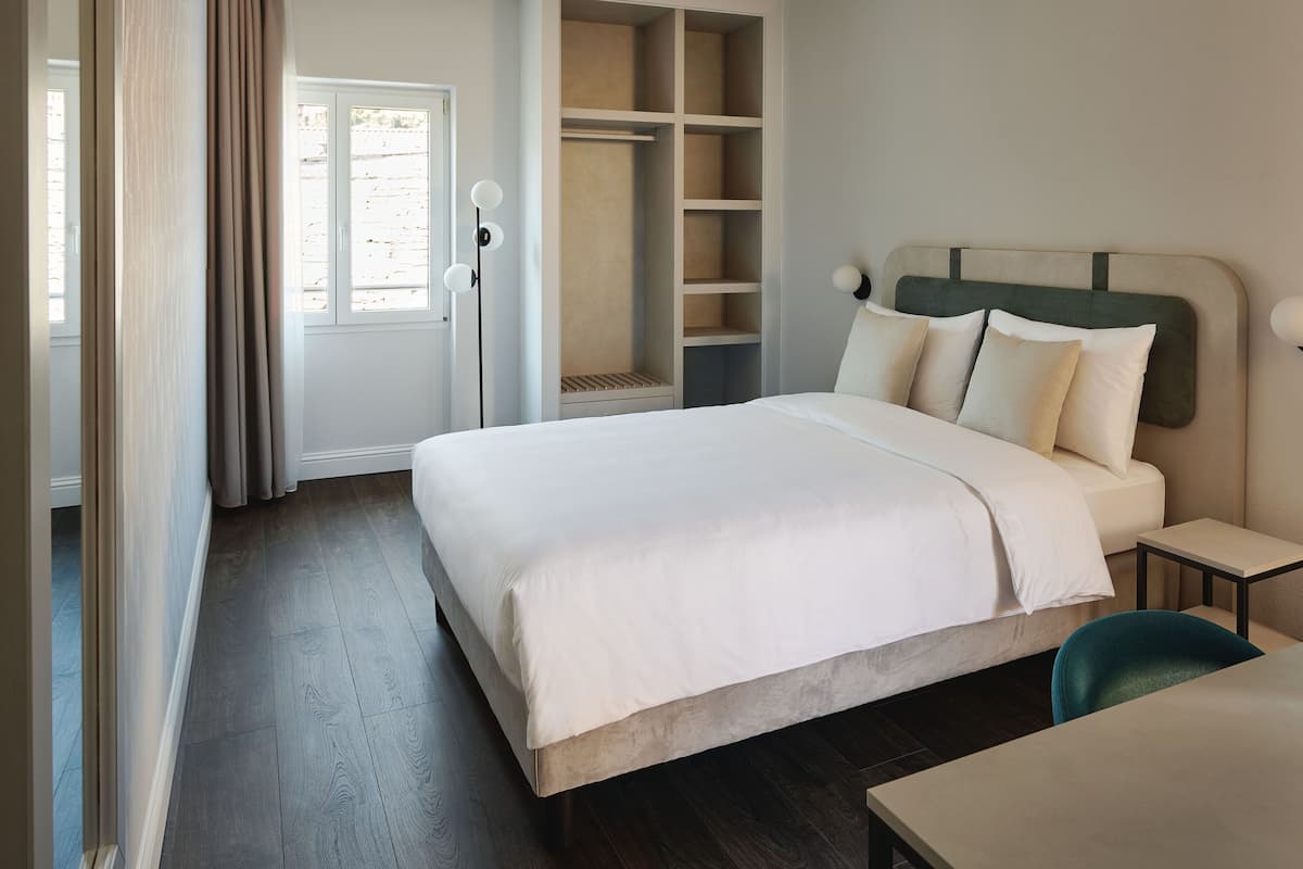 Un dormitorio con cama, mesita de noche, silla, armario y escritorio.