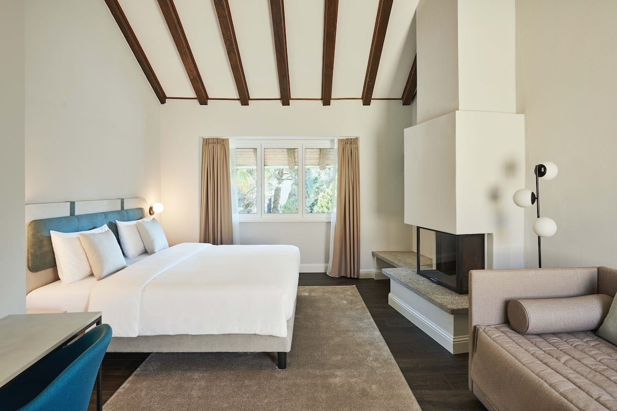 Una habitación de hotel moderna con una cama grande, televisión, zona de estar y ventana con cortinas.